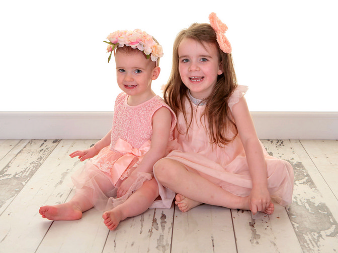 Dressed in gorgeous peach pink dresses, two sisters sit on the floor together