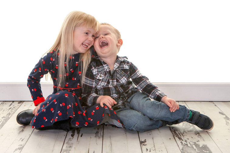 A happy photo of brother a sister laughing together while sat on the floor